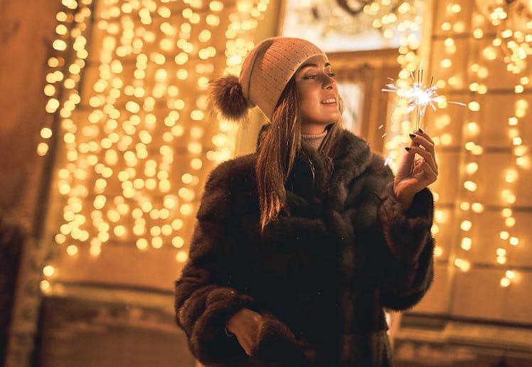 Beautiful girl holding a sparkler enjoys Christmas mood in old European city on festive golden yello...