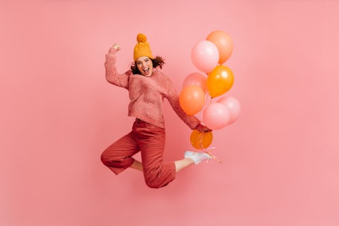 Positive girl in hat jumping and laughing. Blissful young woman dancing with party balloons.