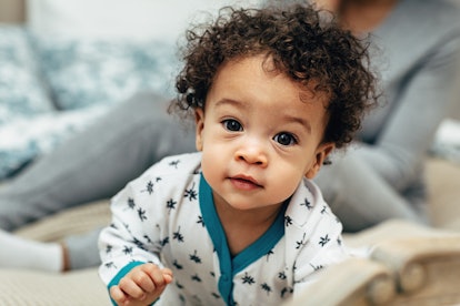 Close up portrait of a curly-haired baby boy crawling on bed