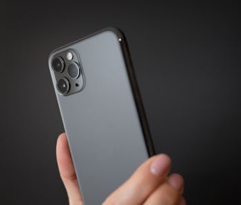 Person holding modern smartphone with triple-lens camera against dark background