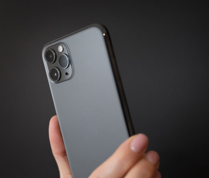 Person holding modern smartphone with triple-lens camera against dark background