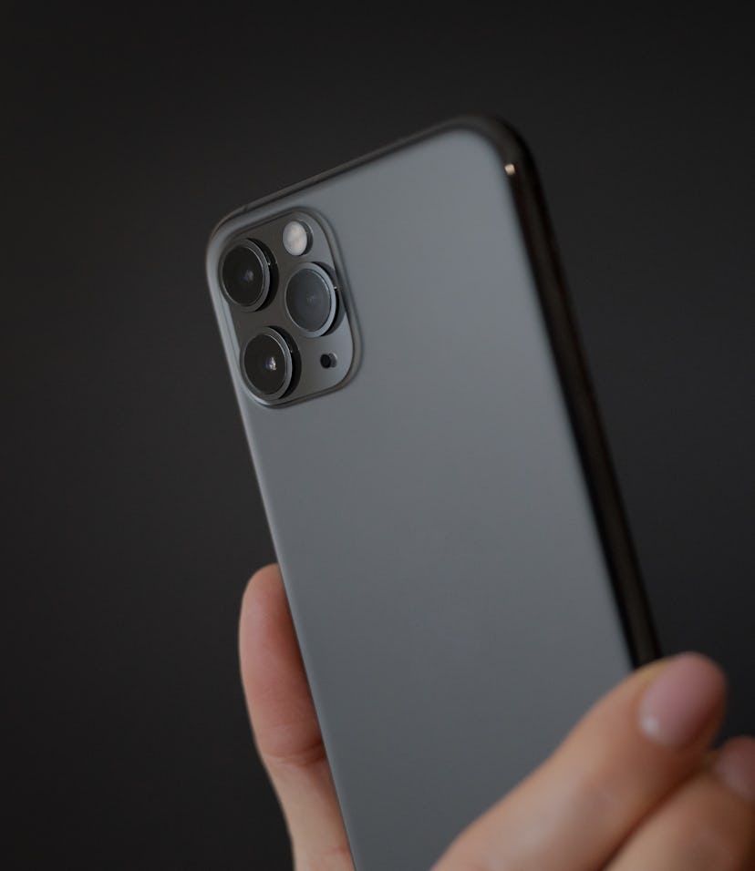 Person holding modern smartphone with triple-lens camera against dark background