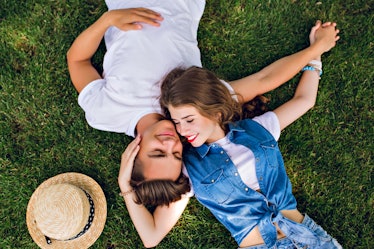 Romantic couple of young people lying on grass in park. They lay on the shoulders of each other and ...