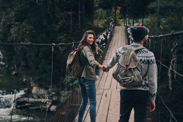 Making each other happy. Young smiling couple holding hands while walking on the suspension bridge