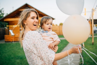 A happy blonde woman holds her nephew and some balloons for his birthday party.