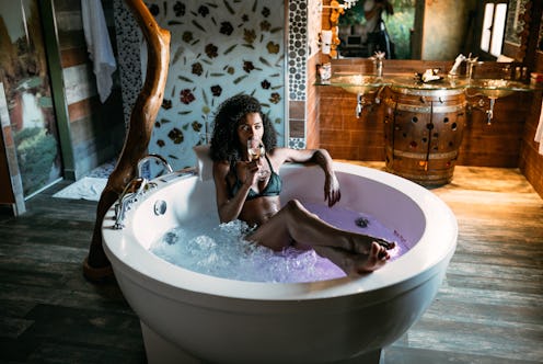 Happy black young woman relaxing in the hydro massage bath drinking wine