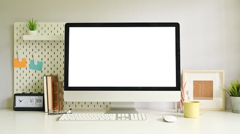 Computer empty screen on creative workspace with peg board and office supplies.