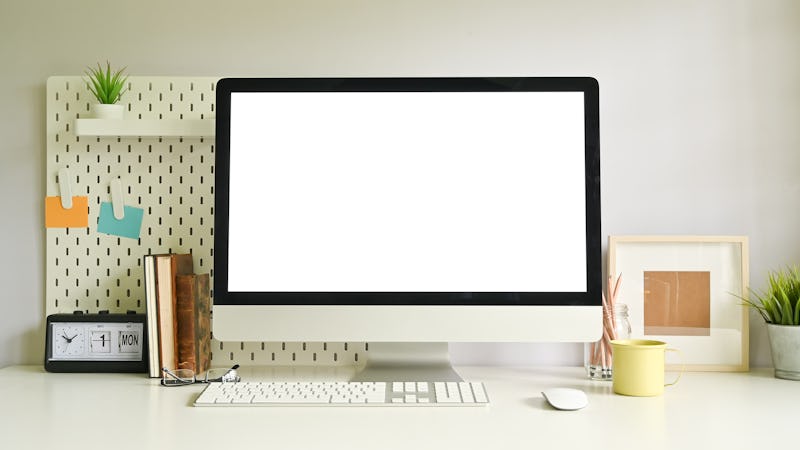 Computer empty screen on creative workspace with peg board and office supplies.