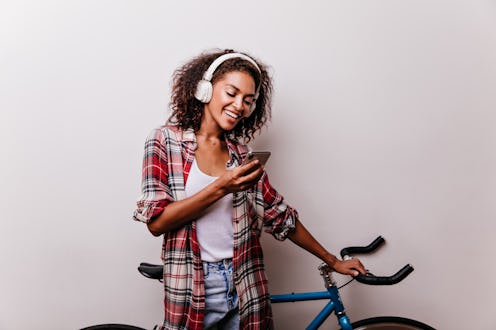 Enchanting stylish woman in headphones reading phone message. Well-dressed african girl with bicycle...