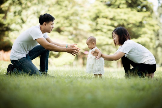 Happy young family spending time together outside, baby walking on the grass