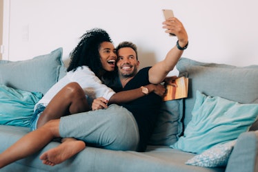 A young couple takes a selfie on their phone while sitting on the couch. 