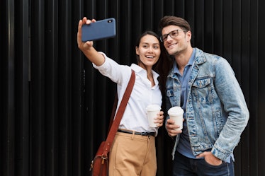 A stylish couple takes a selfie on a phone while out in the city for a coffee date.