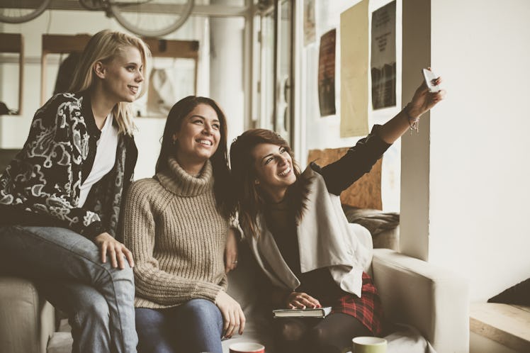 A group of friends take a picture on their phone in the middle of a coffee shop in the winter.