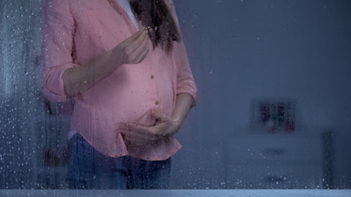 Pregnant lady holding engagement ring on rainy day