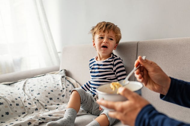 Unhappy child refusing to eat at home with white background while father is trying to deceive the to...