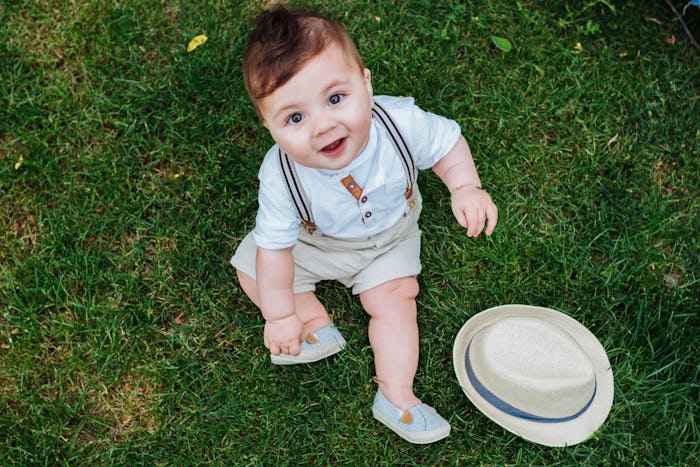 Top view of beautiful baby boy sitting on the grass dressed in a vintage look and looking at the cam...