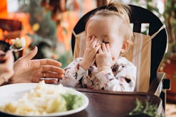a little girl sitting in a highchair covering her face with her hands
