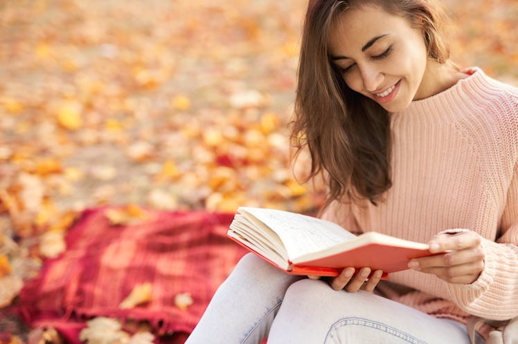 Close up portrait of cute smiling woman woman in autumn park with fall colorful background, sitting ...