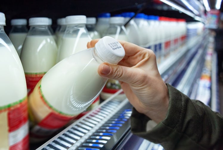Womans hand holding milk bottle in supermarket. Man shopping milk in grocery store. Man checks produ...