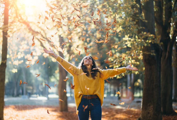 Joyful woman throwing leaves in autumn, having the best week of October 11, 2021, per her zodiac sig...