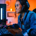 Pretty and Excited Black Gamer Girl in Headphones is Playing First-Person Shooter Online Video Game ...