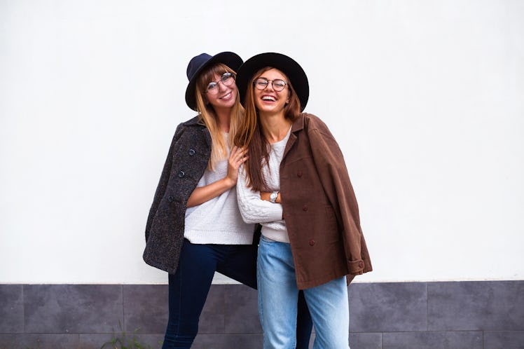 Image of two young happy women friends standing over white wall. Looking at camera.Outdoor portrait ...