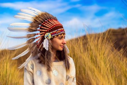 Beautiful young woman in black dotted white chief style Native American headdress during sunset
