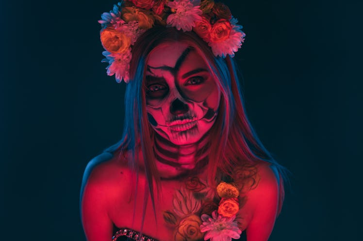 Scary lady with floral wreath and skeleton body art looking at camera during Day of the Dead carniva...