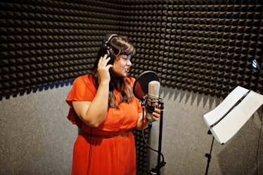 Young asian singer with microphone recording song in record music studio.