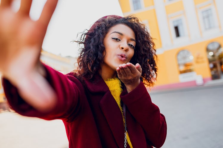 Joyful  African woman with wavy hairs making self portrait over  street background. Perfect smile . ...