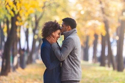 African american young man kissing his girlfriend forehead while walking in autumn city park, copy s...