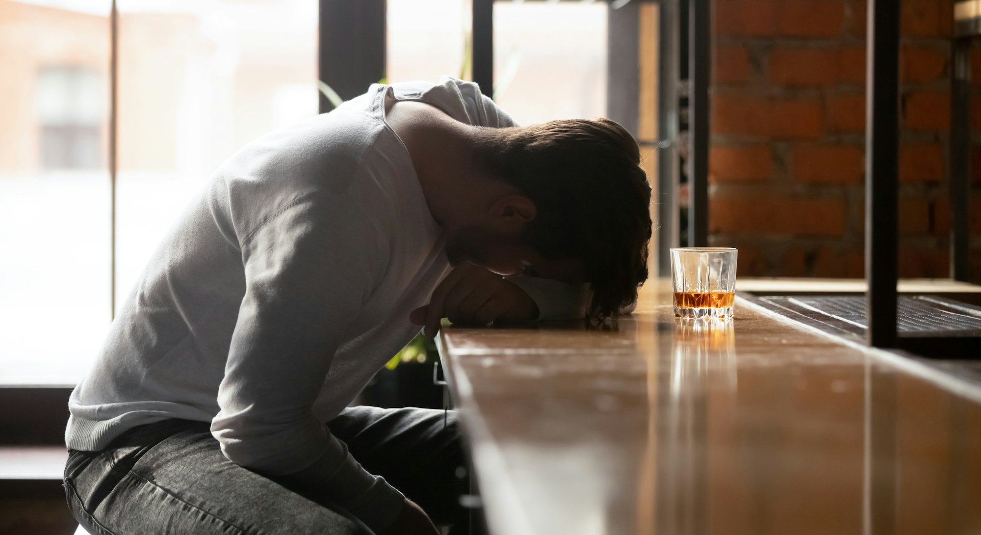 Depressed drunk young addicted man drinker sleeping alone on bar counter with whiskey glass, sad guy...