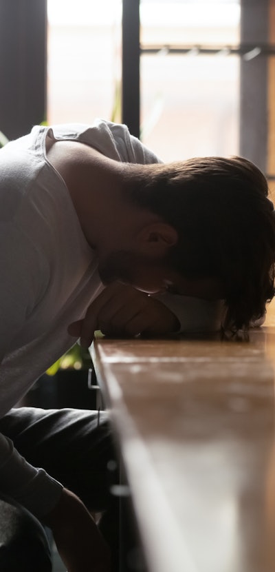 Depressed drunk young addicted man drinker sleeping alone on bar counter with whiskey glass, sad guy...