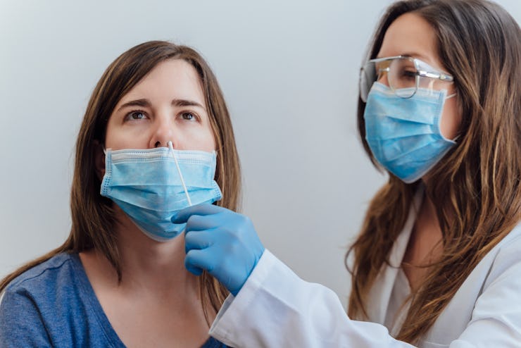 A doctor in a protective suit taking a nasal swab from a person to test for possible coronavirus inf...