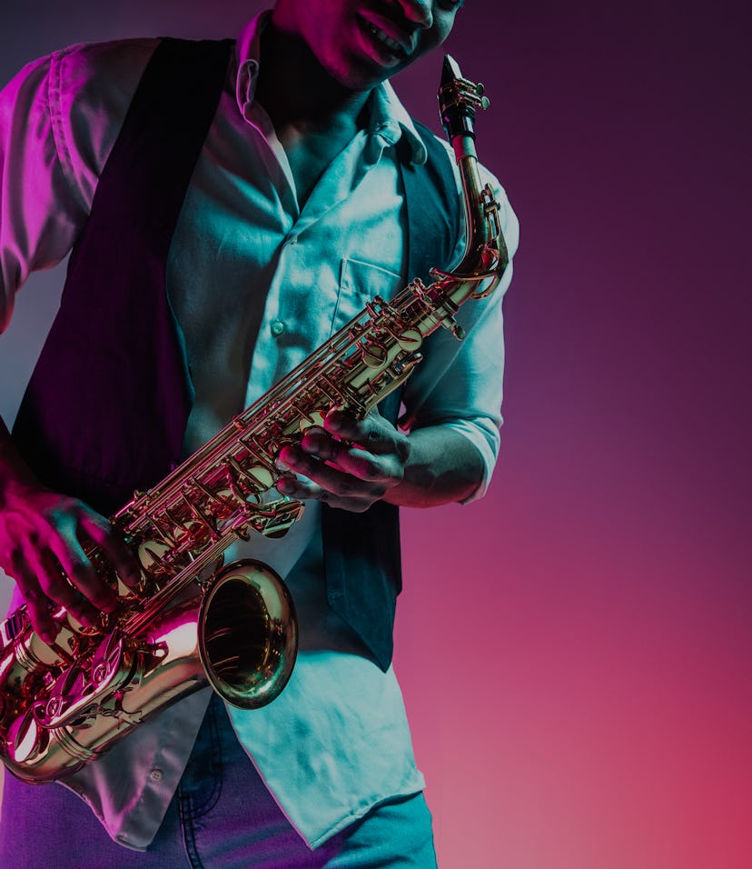 An African American jazz musician is playing the saxophone in the studio on a neon background.