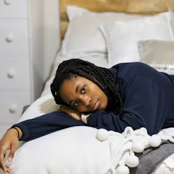A portrait of a beautiful African-American teenaged girl sitting on on her bed and feeling sad and l...
