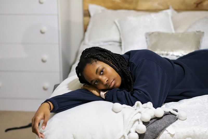 A portrait of a beautiful African-American teenaged girl sitting on on her bed and feeling sad and l...