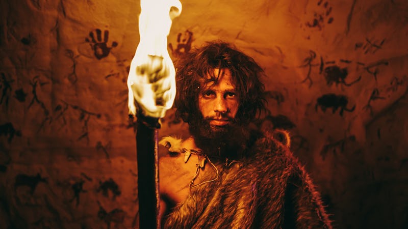 Portrait of Primeval Caveman Wearing Animal Skin Standing in His Cave At Night, Holding Torch with F...