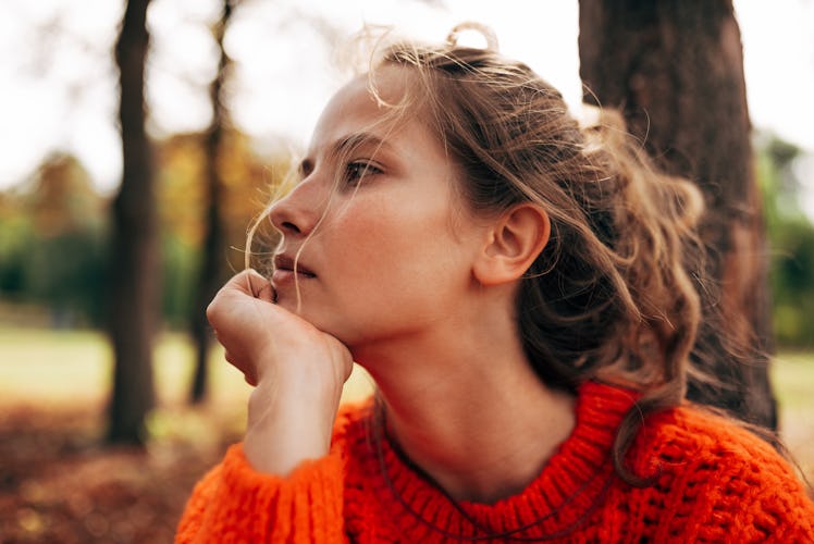 Closeup portrait of pensive womanlooking away, wearing orange knitted sweater posing on fall nature ...