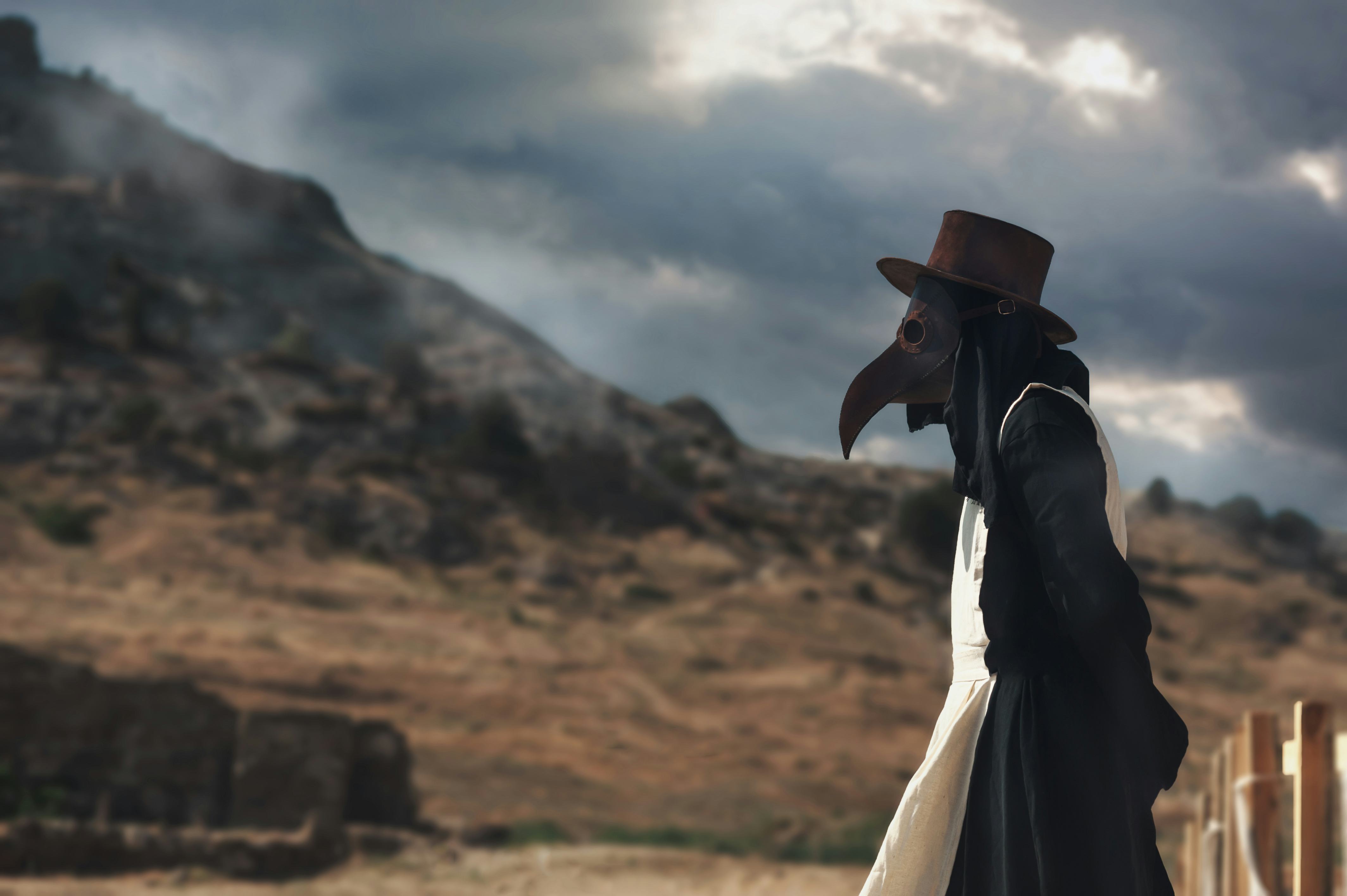 A man in historical masquerade costume of plague doctor in old grange castle near the mountains. Epi...