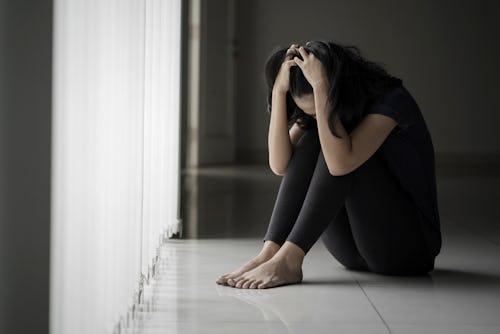 Picture of a desperate woman scratching her head while sitting near the window in black background