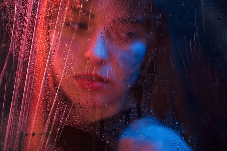 Sad woman. Studio shot in dark studio with neon light. Portrait of beautiful girl behind wet glass.