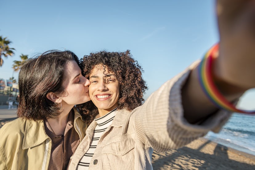 A sweet queer couple takes a kissing selfie on the beach for Instagram.
