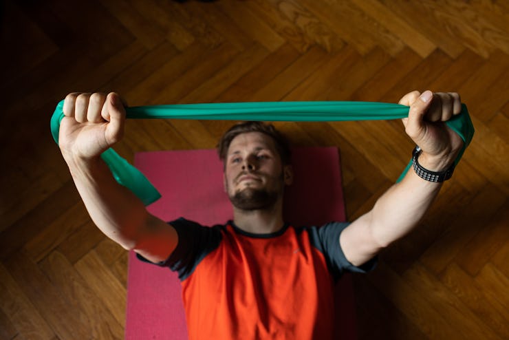 Virtual fitness training, stretching resistance bands exercises online men at home with tablet. Attr...