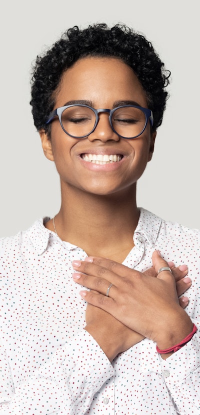 Happy african American girl in glasses isolated on grey studio background keep hands at chest at hea...