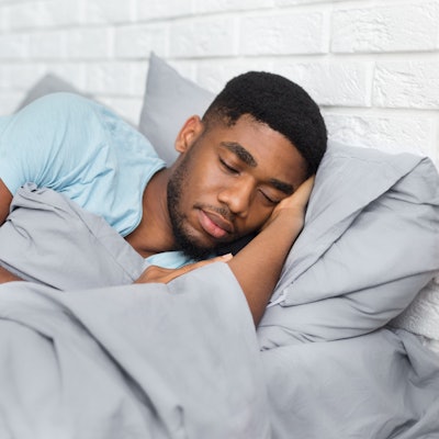 Just resting. Young african-american man sleeping in bed at home, having good dreams, copy space