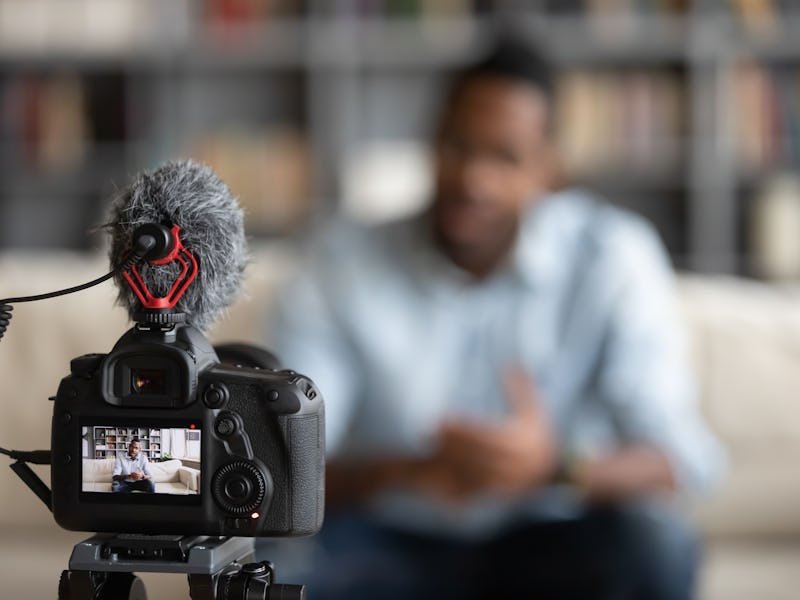 Close up focus of modern professional camera shooting african American male coach or tutor making vl...