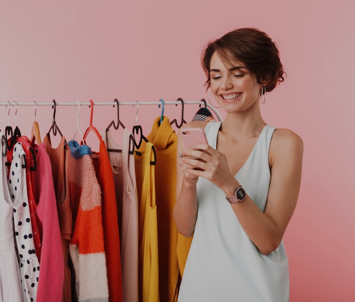 Image of a beautiful happy woman stylist posing isolated over pink wall background near a lot of clo...