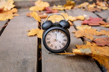 Vintage black alarm clock on autumn leaves. Time change abstract photo. Daylight saving time.
