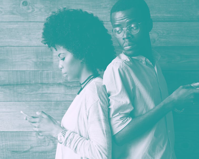 Young African couple standing back-to-back, holding mobile phones. Jealous possessive black man look...